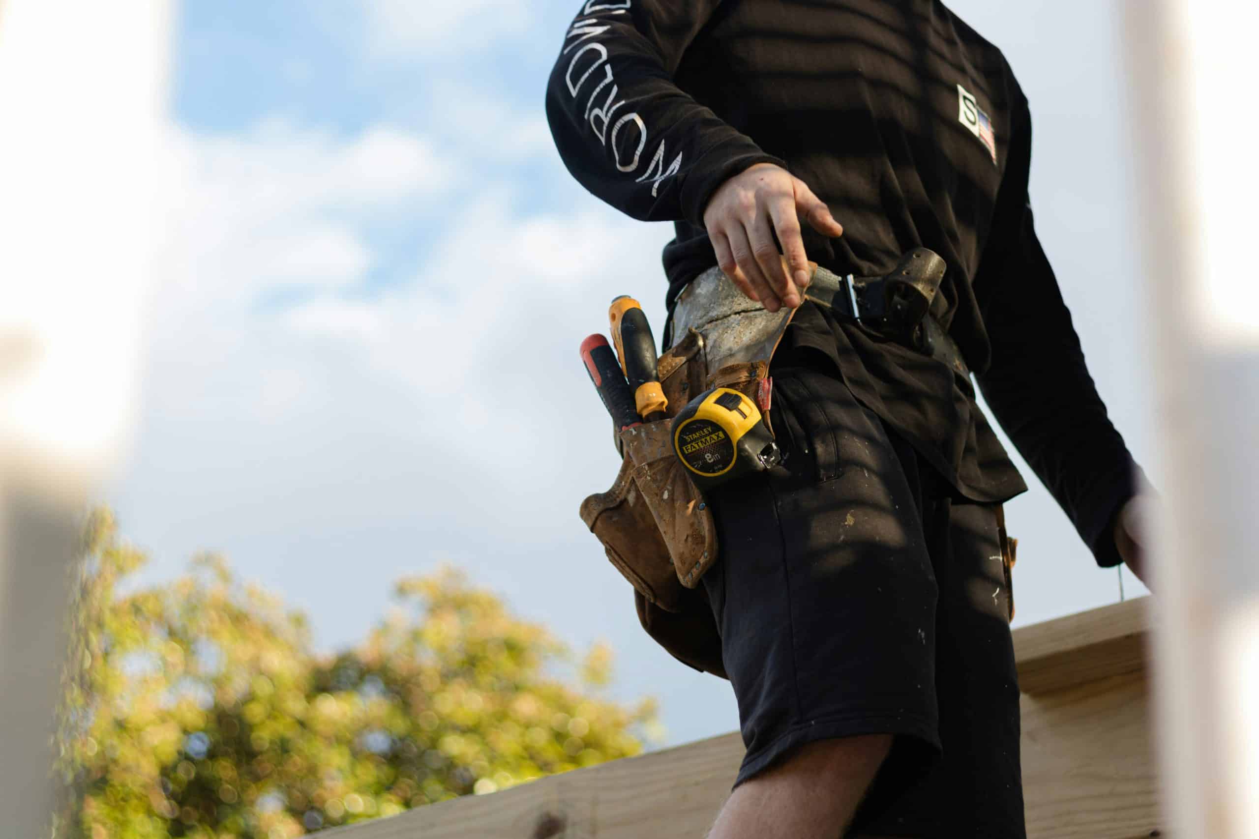 Tradesman walking with tool belt containing screwdriver and tape measure.